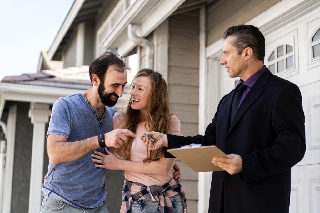A Realtor Broker Sugar Land hands keys to a happy couple outside a modern home with a clipboard.