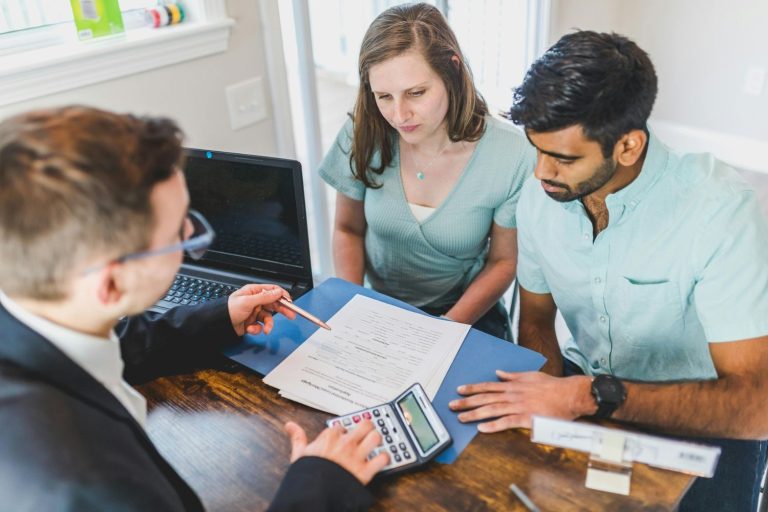 Real estate brokers in Sugar Land reviewing documents and using a calculator with clients at a desk.