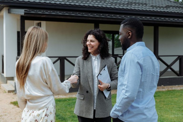 A realtor agent in Sugar Land shaking hands with clients outside a home, holding documents, showcasing real estate services.
