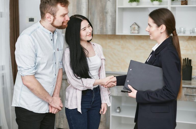 A realtor broker in Sugar Land shaking hands with a couple in a modern kitchen, holding a clipboard, showcasing real estate services.