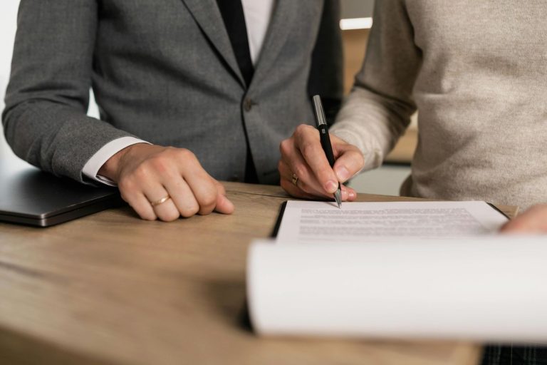 A realtor broker in Sugar Land signing documents at a desk, with a laptop and another person present, symbolizing professional real estate services.