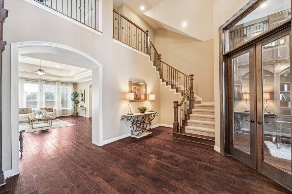 Elegant entryway with rich hardwood floors, grand staircase, arched living room view, and stylish decor, expertly listed by Real Estate Brokers Sugar Land.