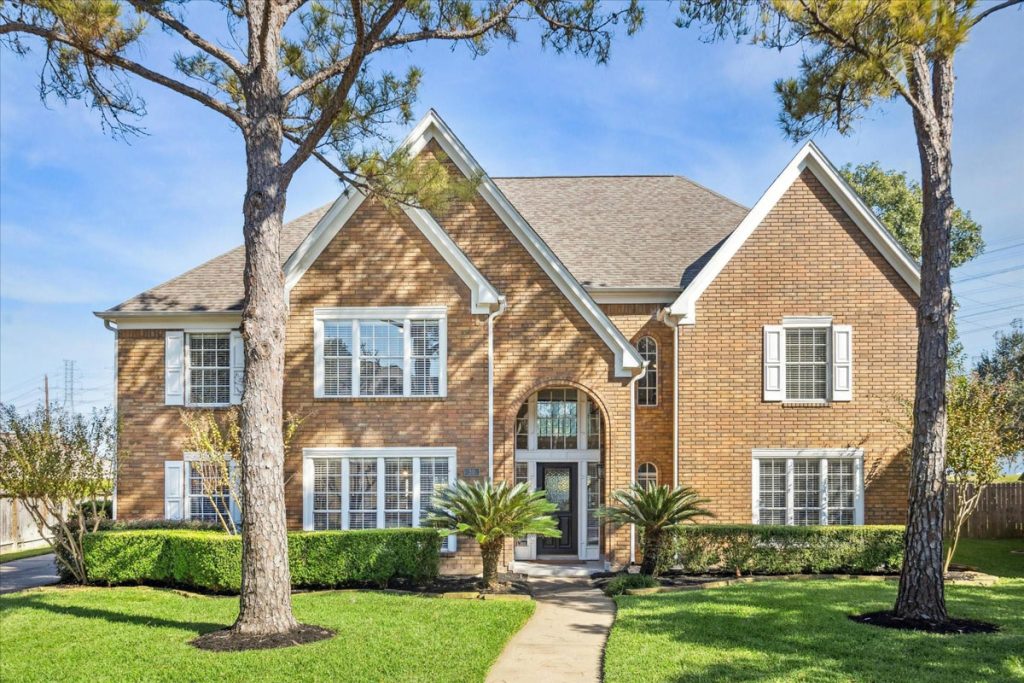 Estate Broker Sugar Land showcases two-story brick home with arched entry, lush landscaping, and symmetrical design.