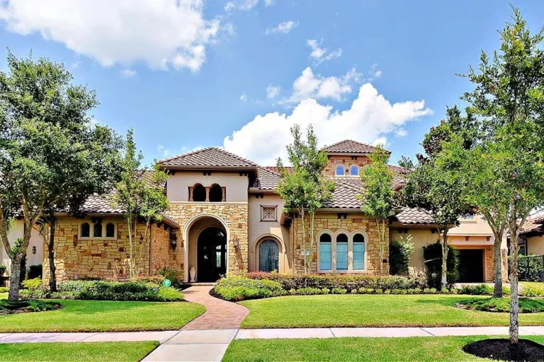 Elegant Mediterranean-style home with stone exterior, arched entry, and lush landscaping, presented by licensed real estate broker in Sugar Land.