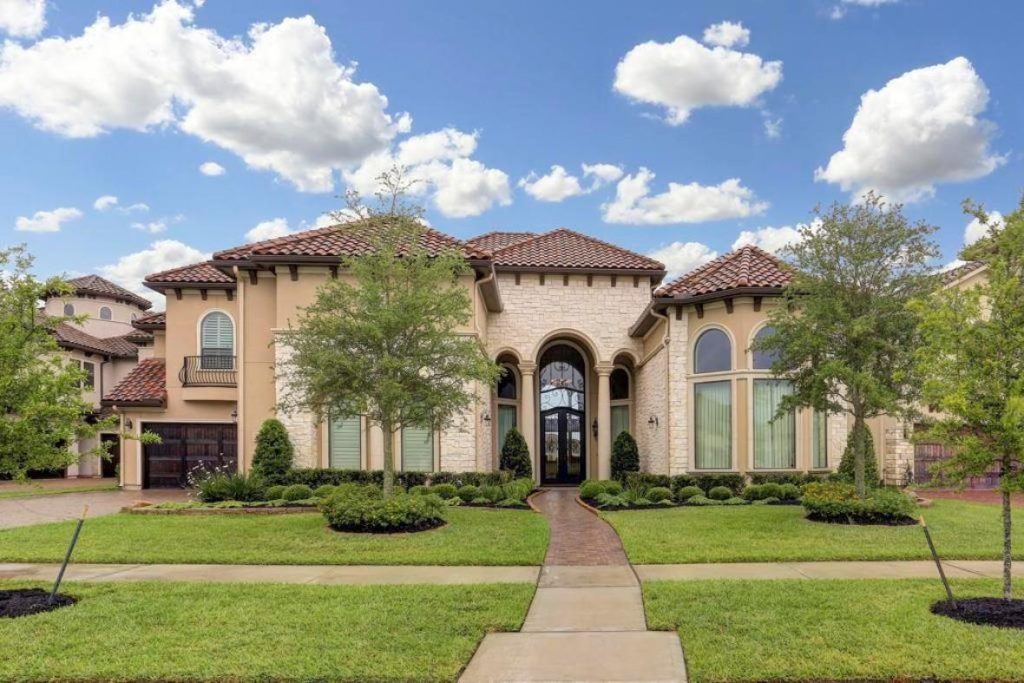 Elegant two-story Mediterranean home with stone entry, tile roof, arched windows, and manicured lawn; home selling agents sugar land