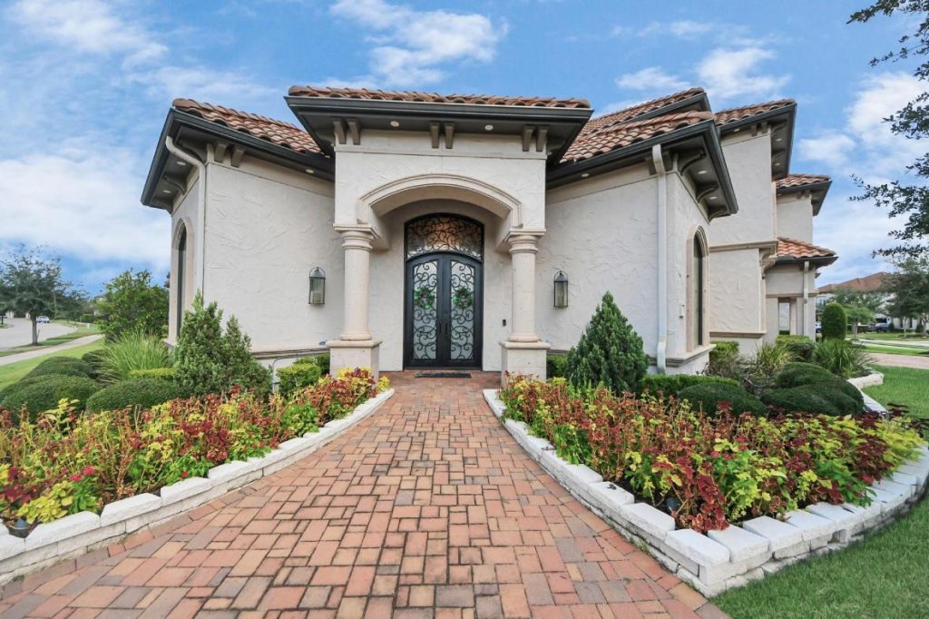 Mediterranean stucco home with arched windows, wrought iron double doors, manicured landscaping—licensed real estate agent sugar land
