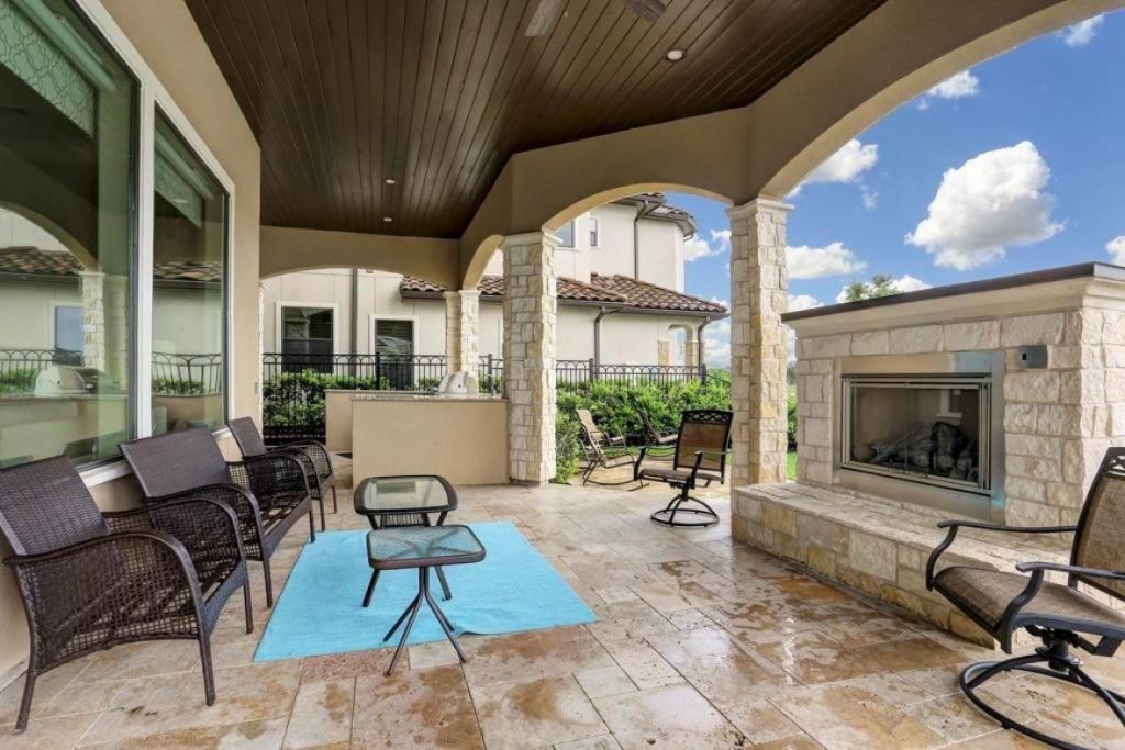Covered patio with stone fireplace, wicker seating, ceiling fan, and arched windows; upscale outdoor living; home selling agents sugar land
