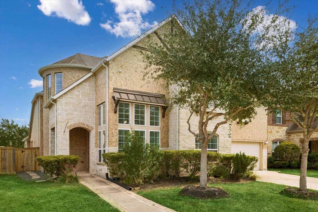 Two-story brick and stone home with arched entry, turret, and manicured lawn; estate broker sugar land for luxury listings and tours