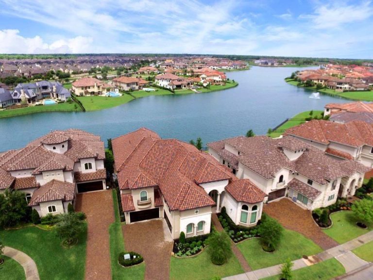Aerial of upscale Sugar Land lakefront community with red-tile roofs, fountain, and landscaped lots, by realtor broker sugar land