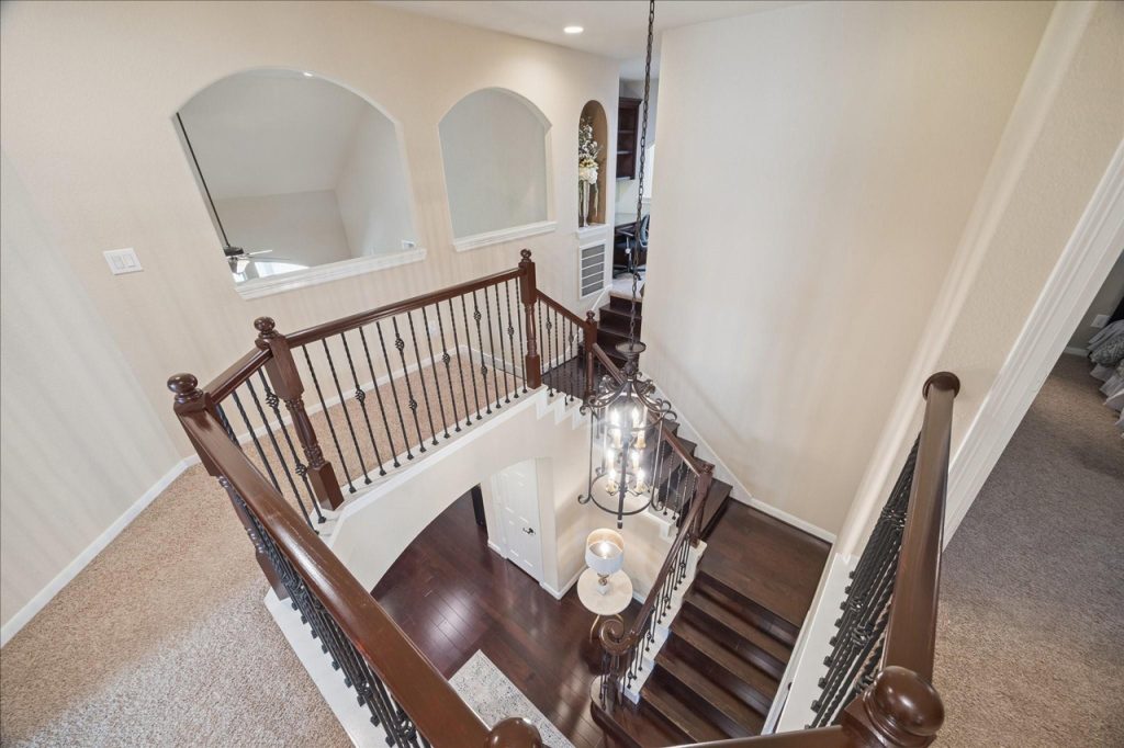 Aerial view of grand curved staircase with wrought-iron railing, chandelier, and hardwood steps in upscale residence marketed by Home Selling Agents Sugar Land.