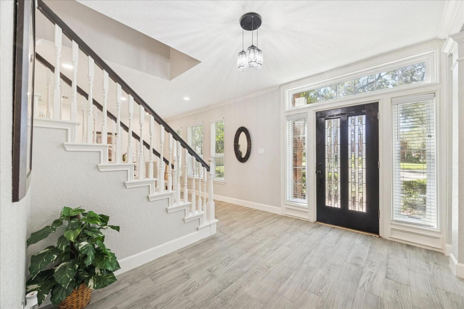 Bright foyer with grand staircase, white balusters, and stylish front door entryway in upscale home, available for viewing at glass pipes Sapulpa location.
