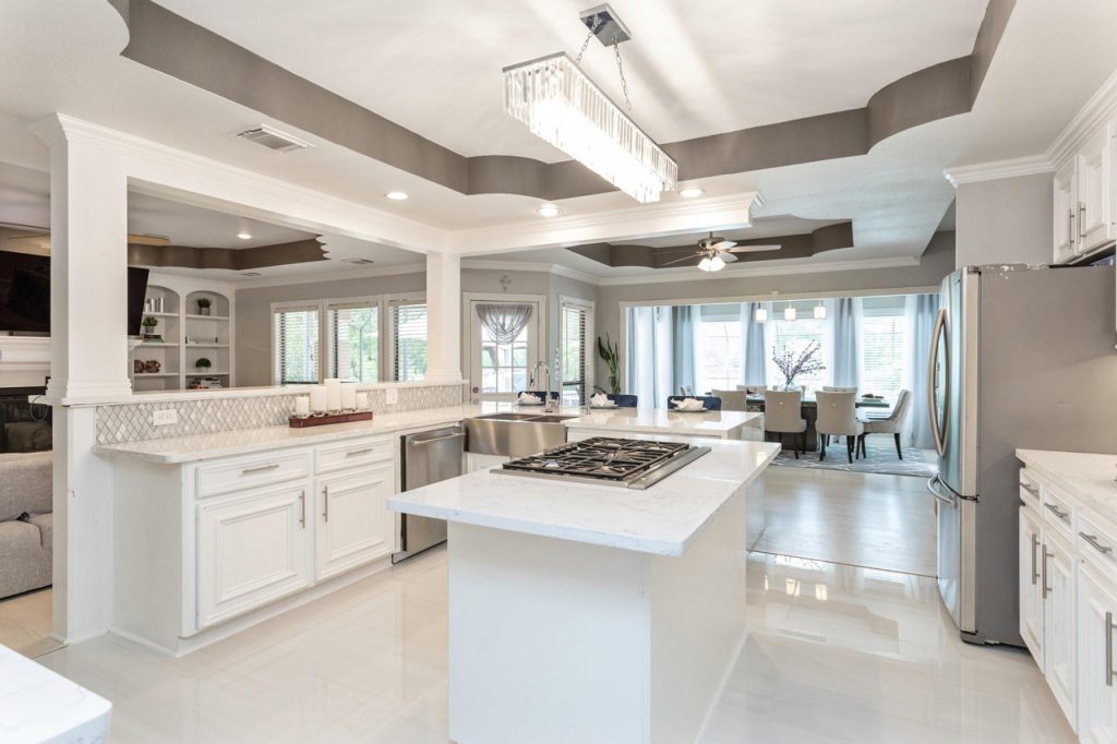Bright open concept kitchen and dining area with marble island, white cabinets, and crystal lighting marketed by House Realtor Sugar Land.