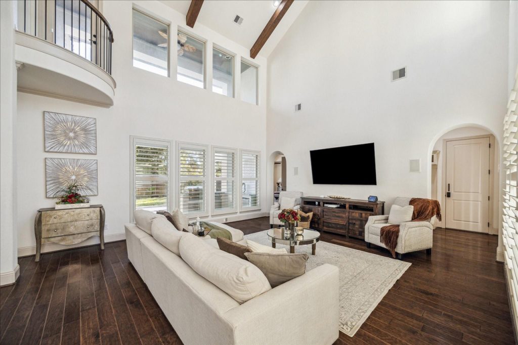 Elegant living room with vaulted ceiling, beams, sectional sofa, and large windows featured by Real Estate Brokers Sugar Land.
