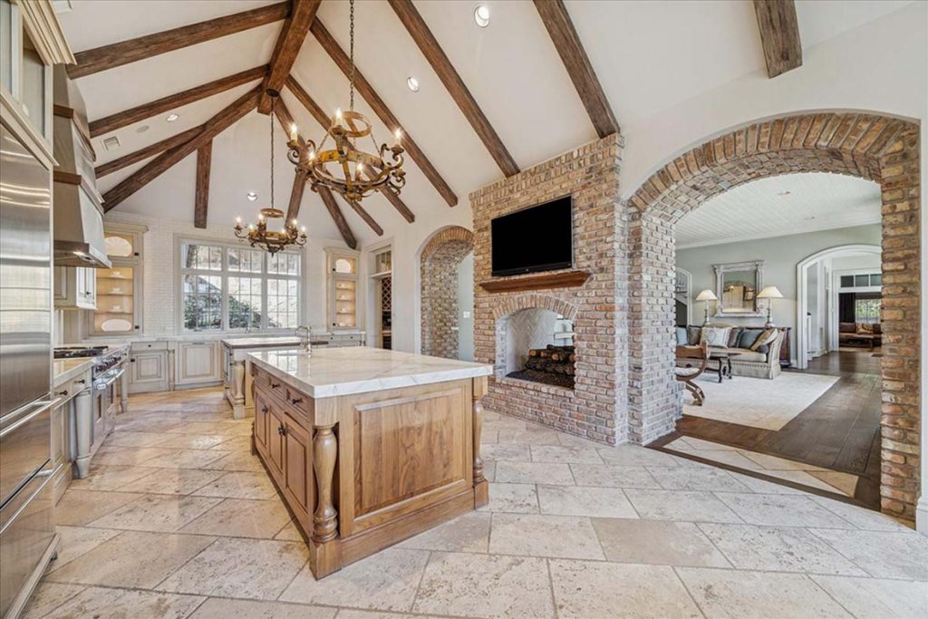 Elegant Sugar Land kitchen with marble island, exposed beams, and brick arch to living room, by real estate agent broker sugar land
