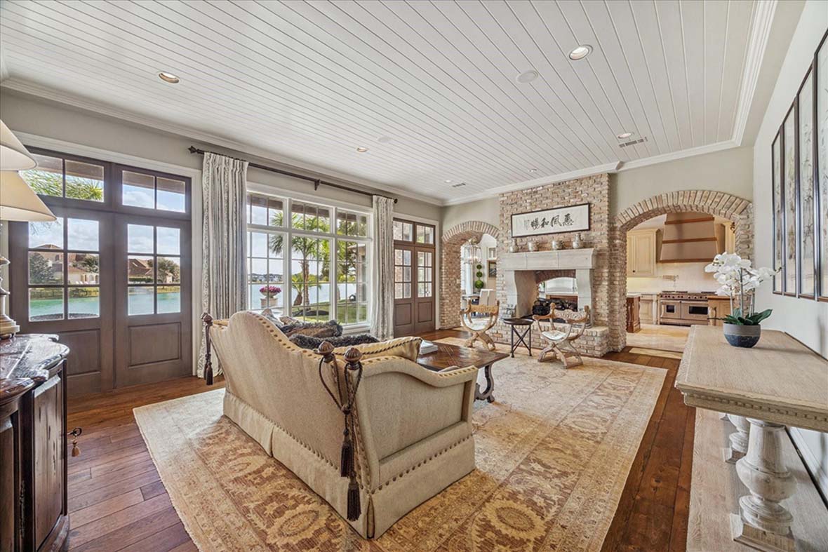 Elegant Sugar Land living room with lake view, stone fireplace, arched kitchen entry, by house realtor sugar land