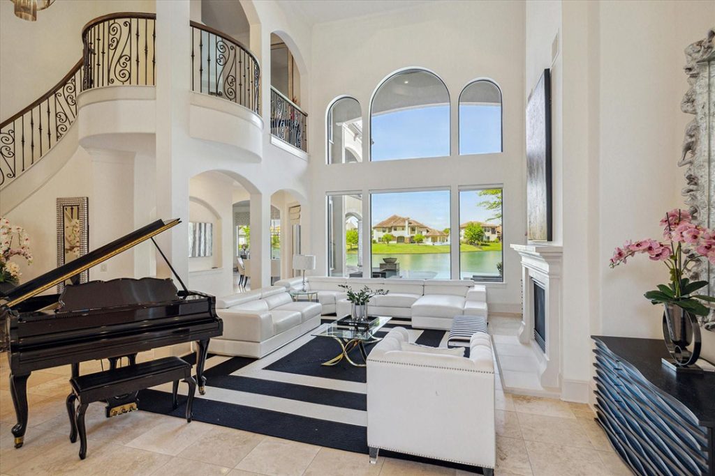 Luxury Sugar Land living room with lake views, grand piano, curved staircase, and fireplace, by realtor broker sugar land