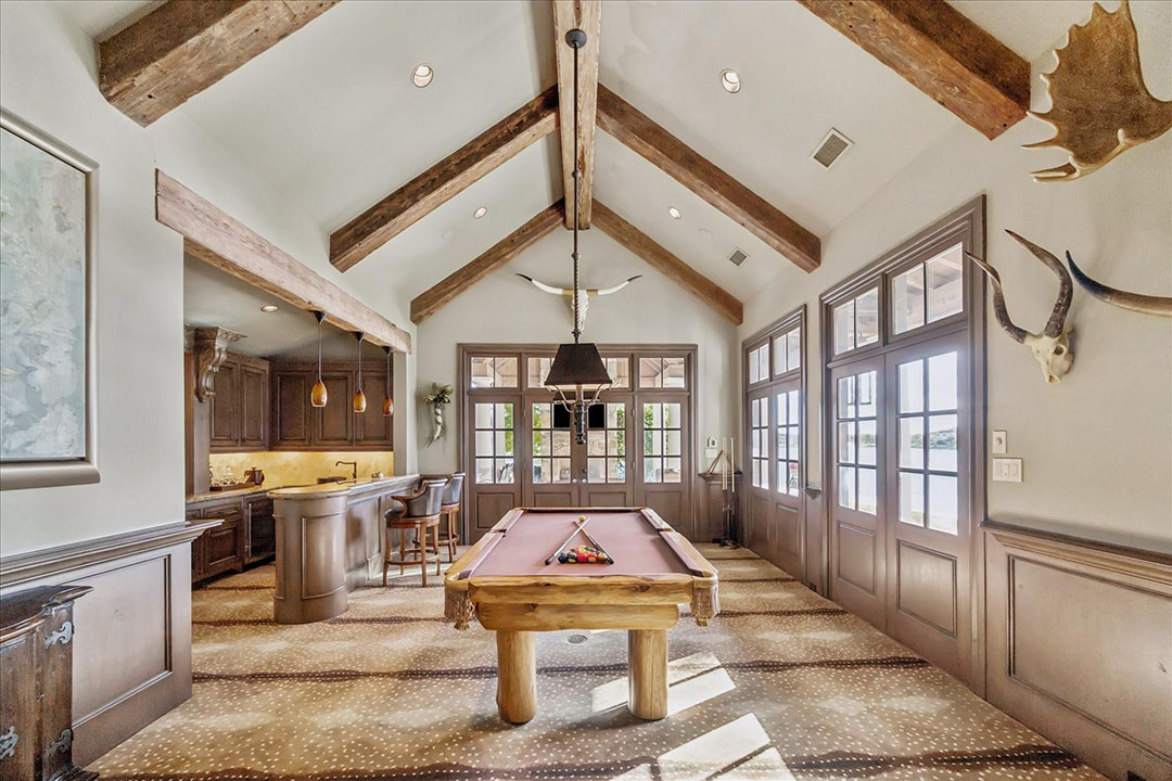 Rustic Sugar Land game room with pool table, bar, and vaulted beams, showcased by real estate agent broker sugar land