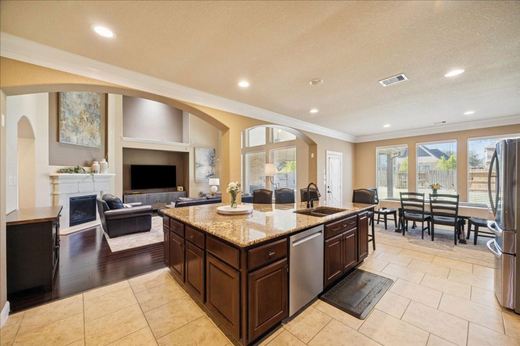 Spacious open-concept kitchen and family room with granite island, hardwood floors, and cozy fireplace in luxurious home listed by Home Selling Agents Sugar Land.