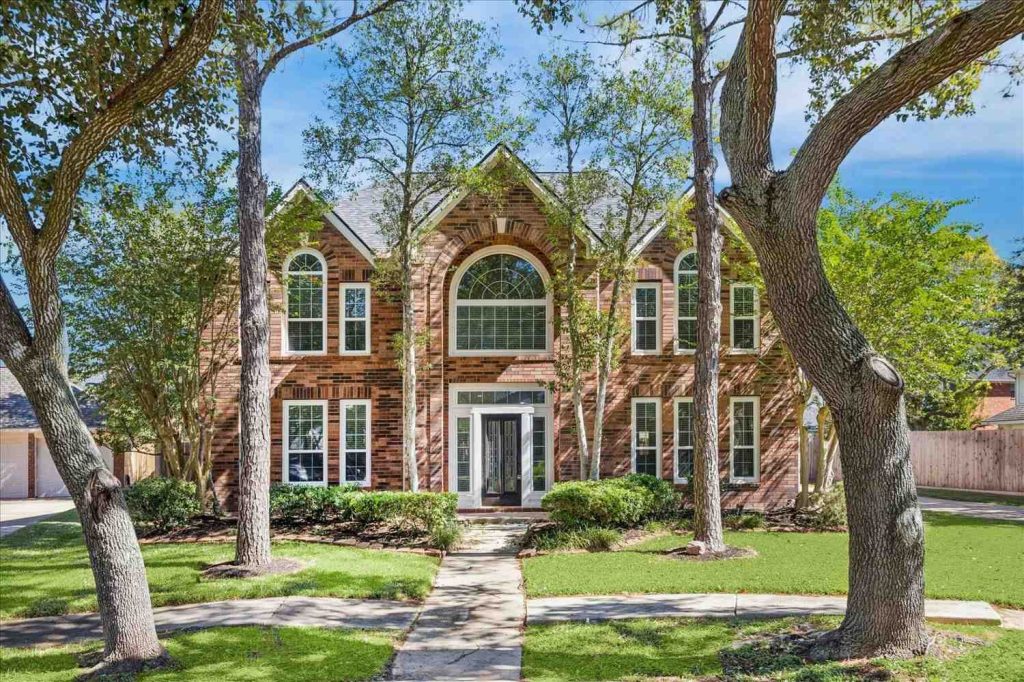 Stunning two-story brick exterior of modern home with arched windows and mature trees, featured at leading glass pipes shop in Sapulpa.