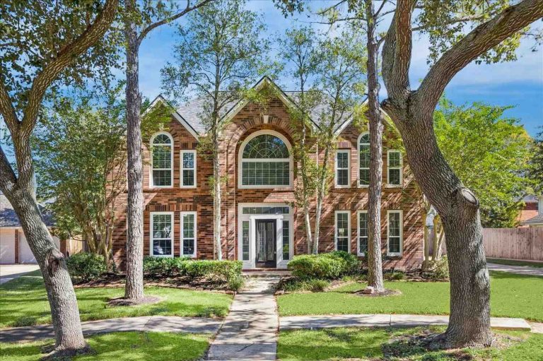 Stunning two-story brick exterior of modern home with arched windows and mature trees, featured at leading glass pipes shop in Sapulpa.