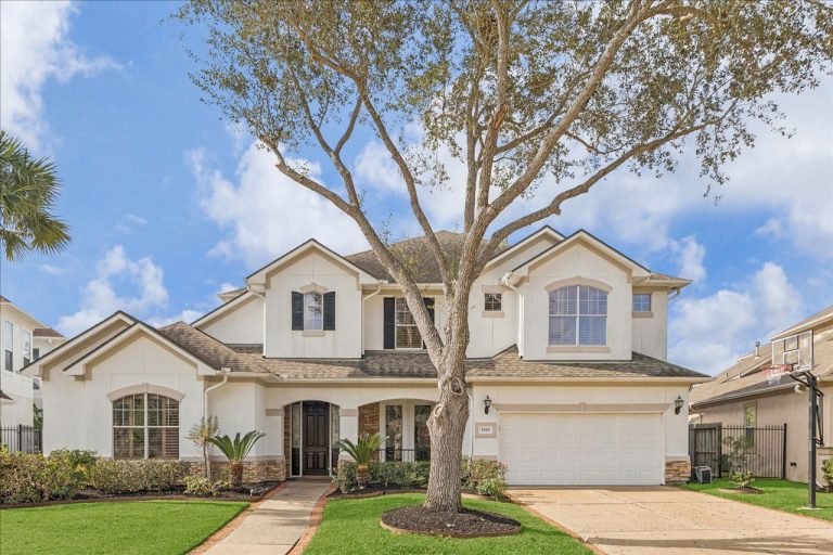 Stunning two-story white brick home with mature tree and manicured lawn, expertly marketed by experienced House Realtor Sugar Land.