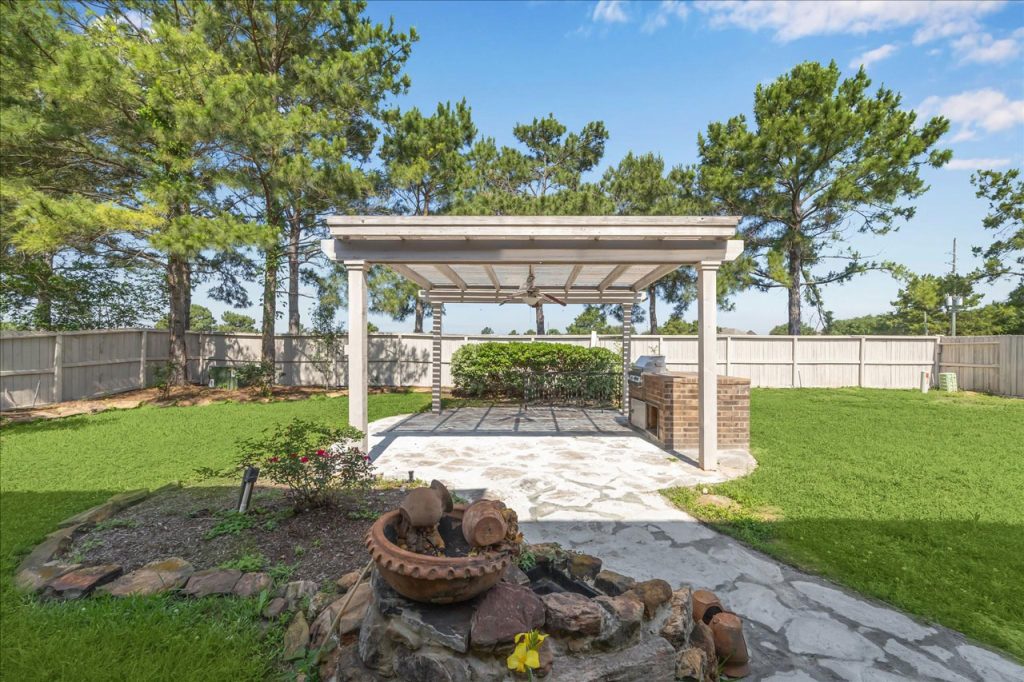 Licensed Real Estate Broker Sugar Land presents shaded backyard with pergola, outdoor kitchen, and terracotta fountain