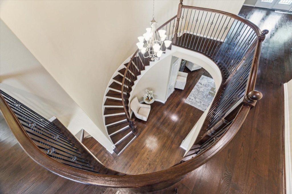 Looking down a stunning spiral staircase with a chandelier, a luxury detail from a licensed real estate broker Sugar Land.
