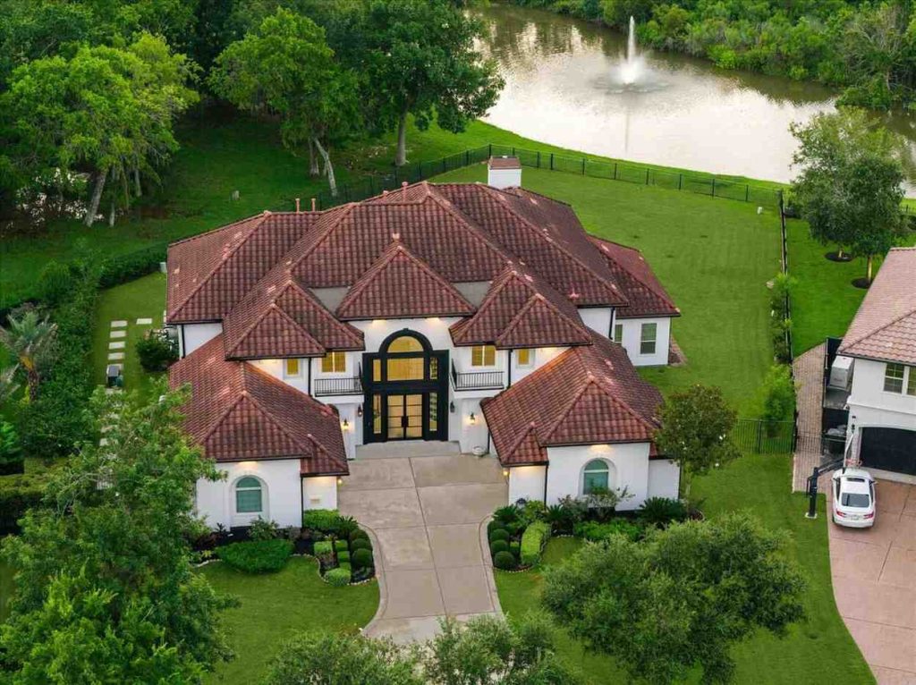 Aerial view of a luxury Mediterranean estate with a tile roof and lake, a prime listing for Realtor agents sugar land.