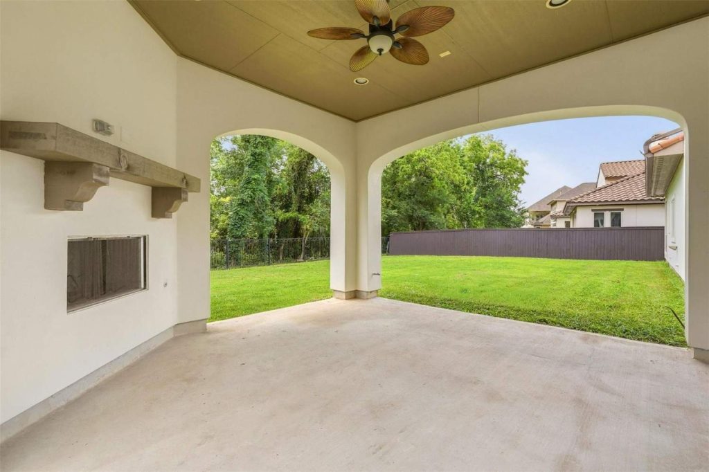 An empty covered back patio with a built-in fireplace and ceiling fan looking out over a fenced backyard, typical of Lease Properties Sugar Land.