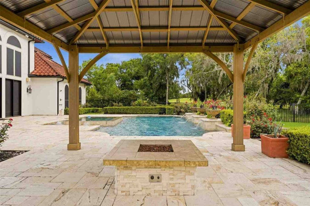 Looking out from a covered gazebo at a luxurious pool and a modern fire pit, showcase property by Realtor agents sugar land.