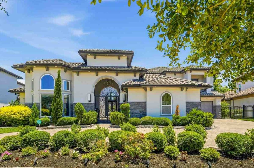 Stunning front view of a modern Mediterranean-style luxury home with detailed landscaping, shown by an estate broker sugar land