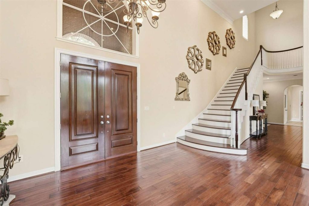 See a stunning two-story home entry with dark wood doors and staircase, curated by your real estate agent Sugar Land.