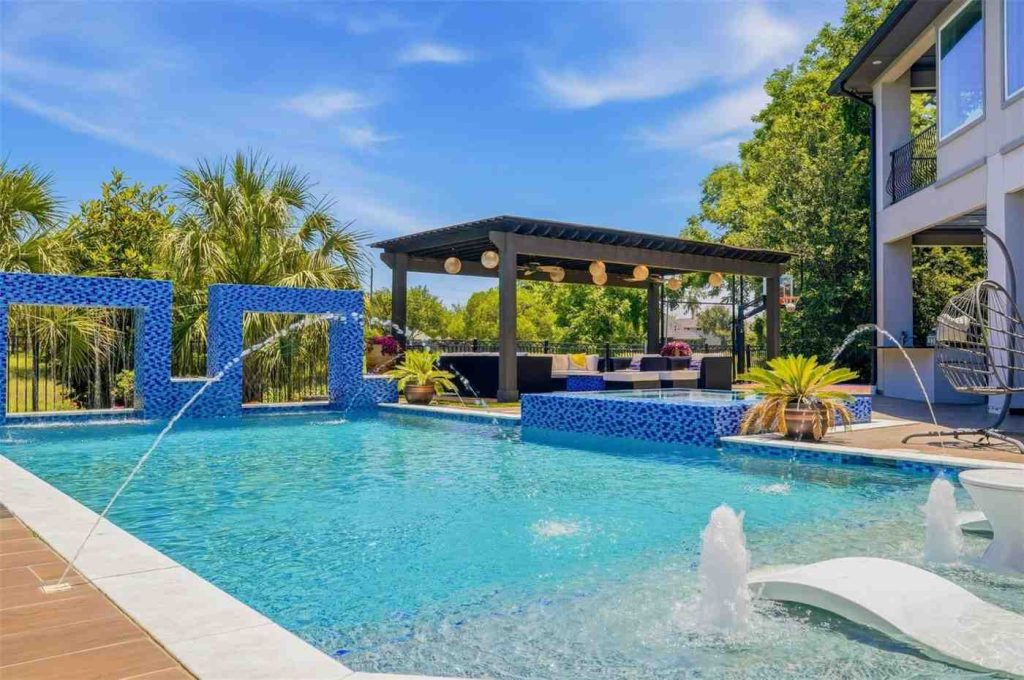 Top-tier custom blue swimming pool with waterfalls and a massive pergola lounge, as shown by an estate broker sugar land