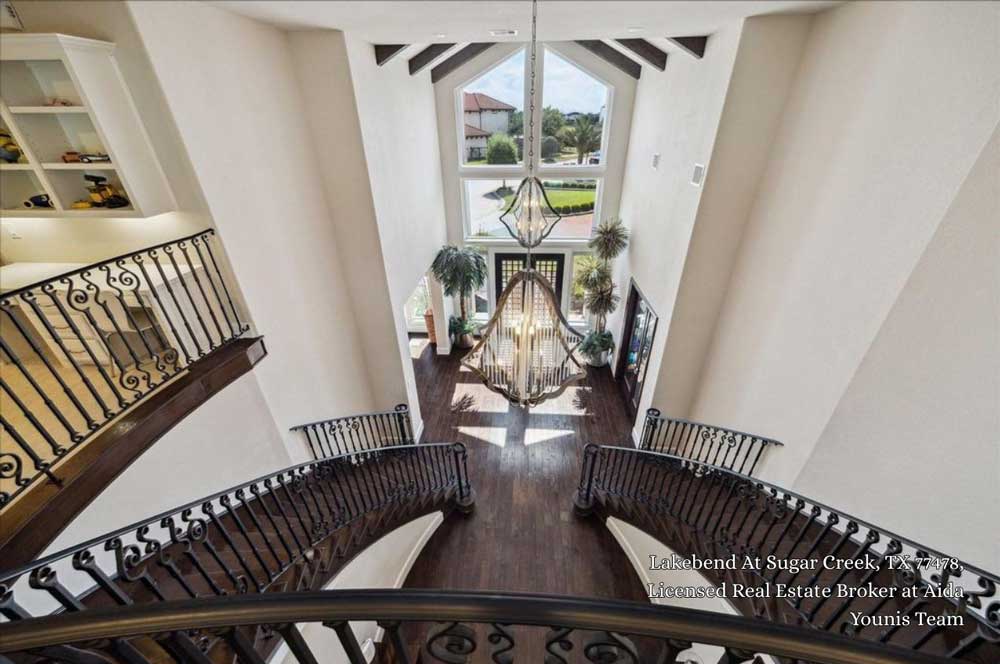 High angle view of a luxury home interior featuring double wrought iron staircases and a grand chandelier.