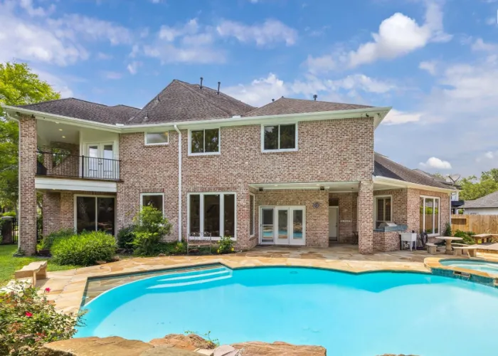 Sparkling backyard swimming pool and spacious stone patio behind 4111 Thistle Hill Court, Sugar Land, TX 77479.