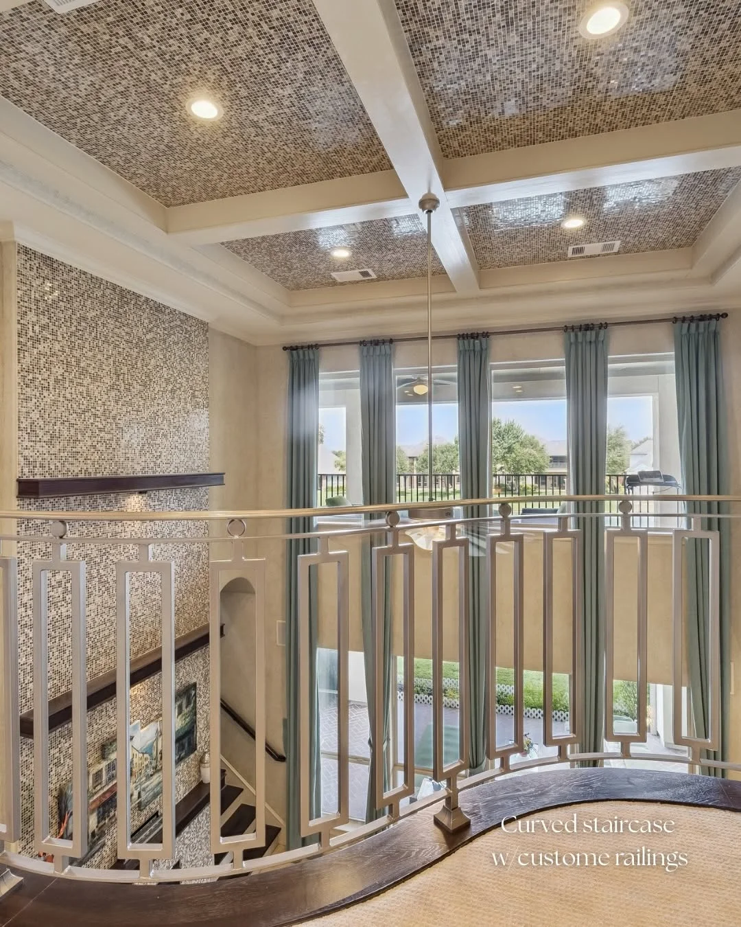 High-angle interior view showing a curved staircase with custom railings in a Riverstone waterfront home for sale.