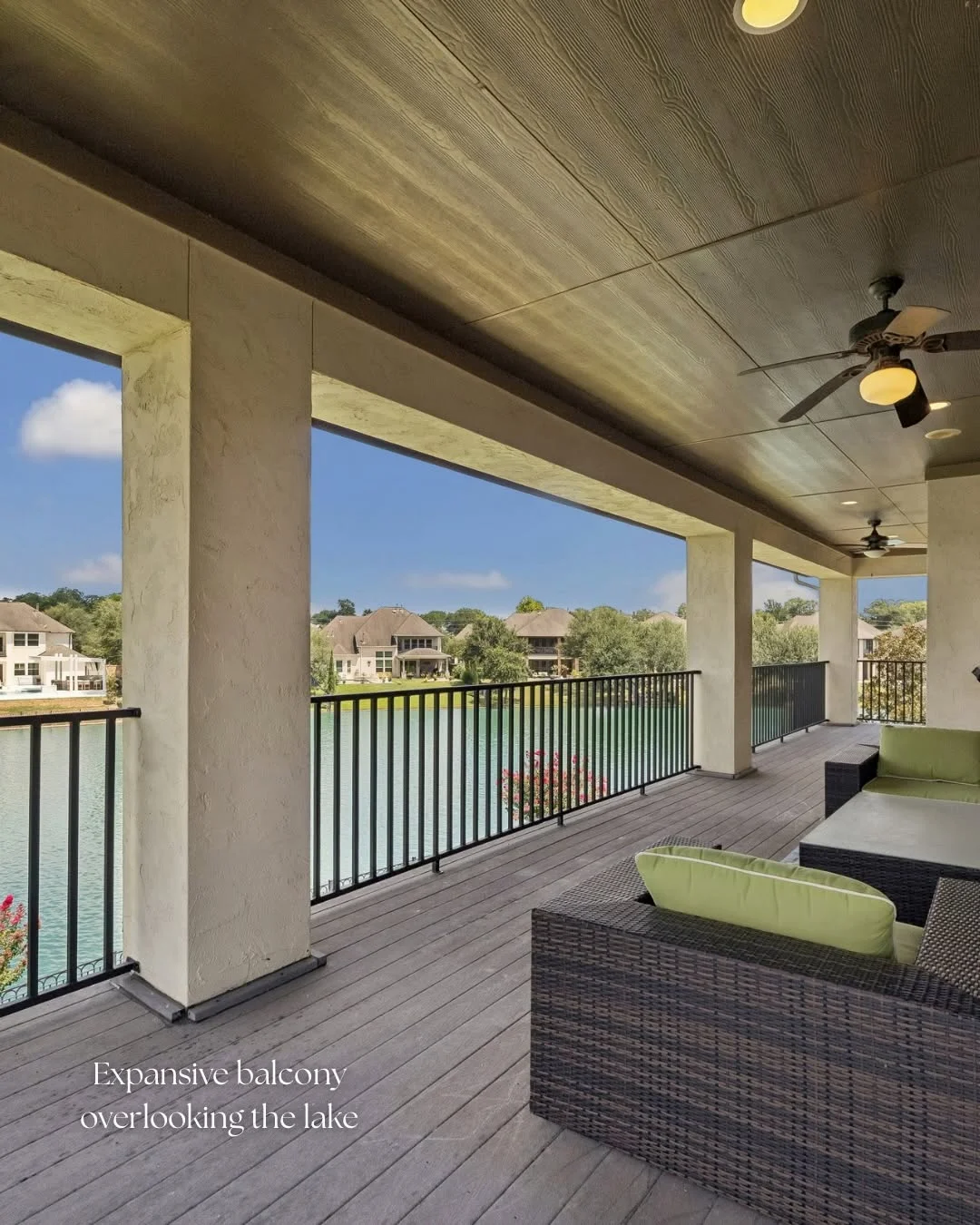 Expansive covered balcony with wicker seating overlooking scenic lake views at a Riverstone waterfront home for sale.