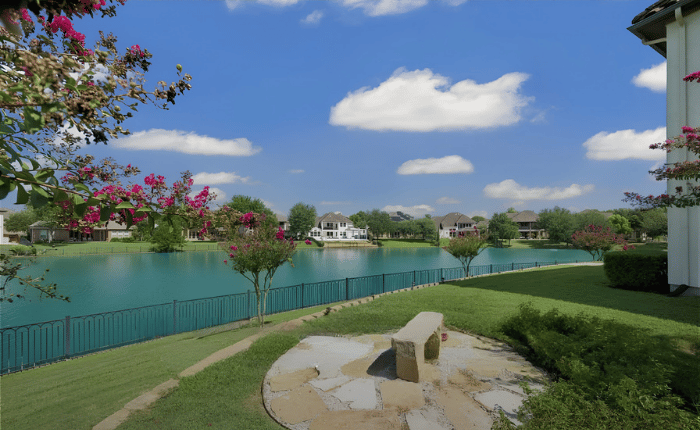 Scenic lake view from a green lawn with a stone bench beside a luxury Riverstone waterfront home for sale.